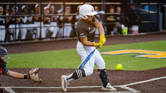 A softball player is at home plate swinging at a softball