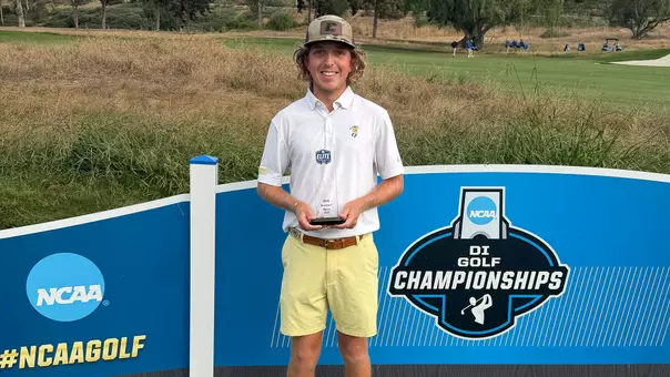 Camden Braidech stands proudly in front of the NCAA Men's Golf Championships signage holding his NCAA Elite Scholar-Athlete Award