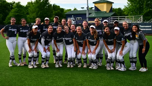 a photo of a team of softball players on the field after a game with a train-shaped building behind them.