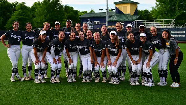 a photo of a team of softball players on the field after a game with a train-shaped building behind them.