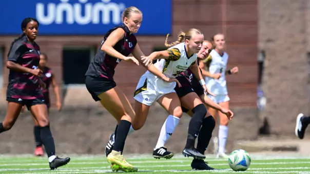 A soccer player in white and a soccer player in black are battling for the ball on the pitch.