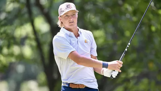 Evan Rogers follows his iron shot tracking the green with his hands in front, waist high, holding an upright club.