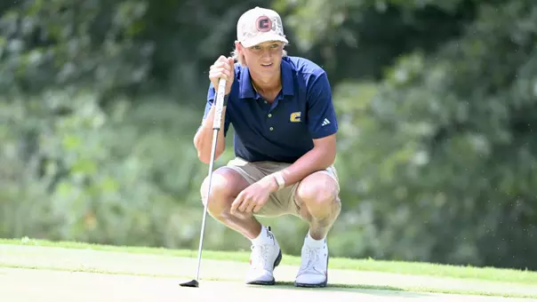 Evan Rogers crouches down reading the green looking left with his putter propped up with his right hand.