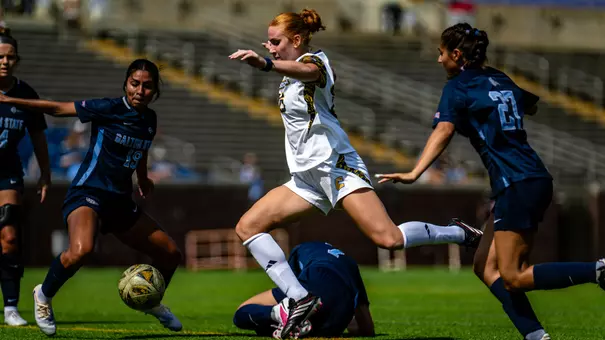 A soccer player in white is dribbling the ball through the defense all in dark colors.
