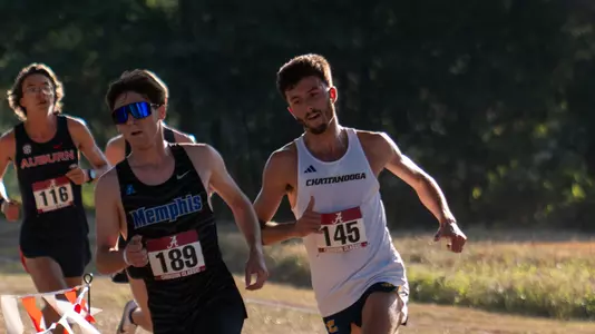 Runners in dark and light uniforms are running a race on a sunny day.