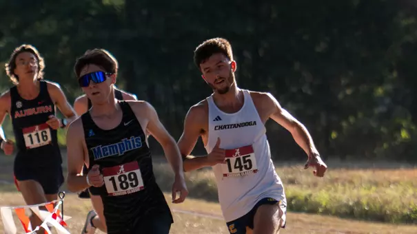 Runners in dark and light uniforms are running a race on a sunny day.