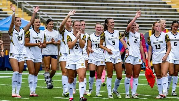 A soccer team in white is waving to the crowd after a game.