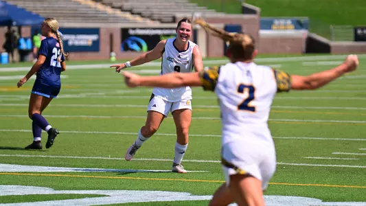 Two soccer players in white are celebrating a goal with arms outstretched.