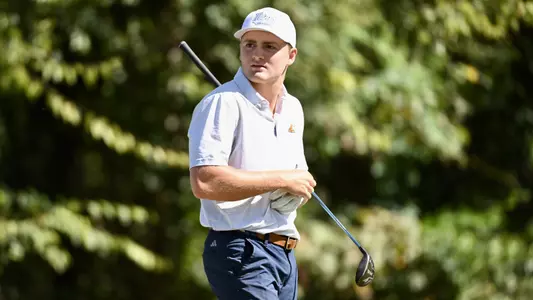 Thad Whitfield walks off the tee with his club under his arm staring down his ball in the distance.