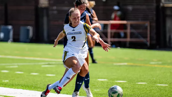 A soccer player in white cuts off the player in black to steal the ball during a match on a sunny day.