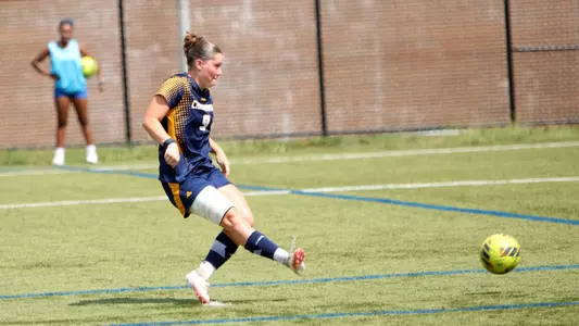 A soccer player in a dark uniform is shooting a penalty kick on the pitch.