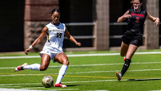 A soccer player in white is kicking the ball on the pitch.