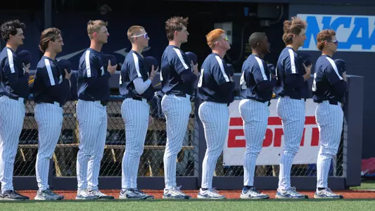 Players on the Toledo baseball team holds their hats and look at the flag during the national anthem