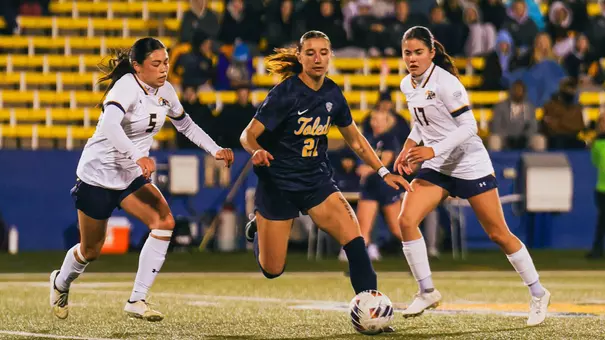 Alli Macbeth dribbles a soccer ball between two defenders against Kent State