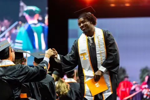 Dylan Sampson fist bumps another graduate while walking during the Spring commencement inside Thompson-Boling Arena at Food City Center on May 15, 2026. Photo by Steven Bridges/University of Tennessee.