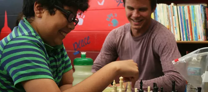 Photo of Josh Ess from Wisconsin men's hockey playing chess with a local child during community service learning and Badgers Give Back