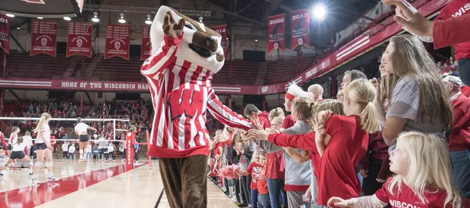 Bucky Badger slaps hands with children lining the volleyball court