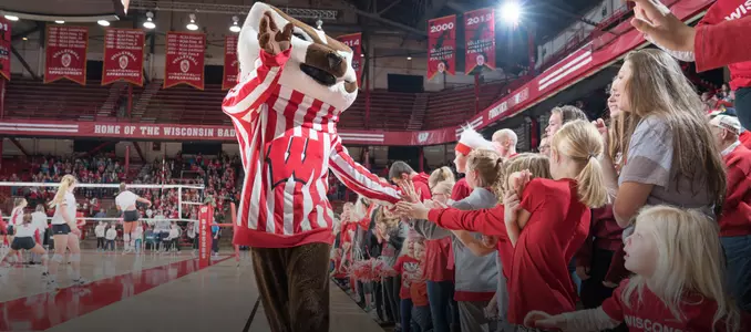 Bucky Badger slaps hands with children lining the volleyball court