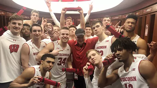 Men's basketball team in locker room with Dave Anderson, motivational speaker, and holding red belts