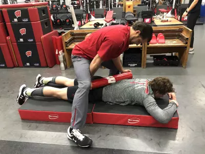 UW Strength & Conditioning Coach Jim Snider rolls a weight over Owen Lindmark to help loosen up muscles