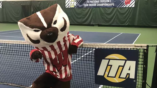 Bucky Badger at the tennis court with banner of ITA Championships