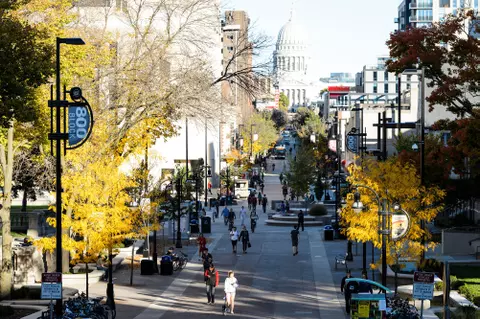 In a view seen from Bascom Hill at the University of Wisconsin-Madison, pedestrians walk past the intersection of Library Mall and State Street Mall during autumn on Oct. 18, 2016. on the horizon at top is the Wisconsin State Capitol building. At left is the Memorial Library. (Photo by Jeff Miller/UW-Madison)