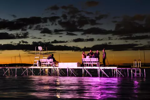 Bathed in the reflection of purple light from the nearby Memorial Union Terrace performance stage at the University of Wisconsin-Madison, a few people linger on a  Terrace swimming pier in Lake Mendota to watch as a summer sunset falls to nighttime on Aug. 31, 2016. (Photo by Jeff Miller/UW-Madison)