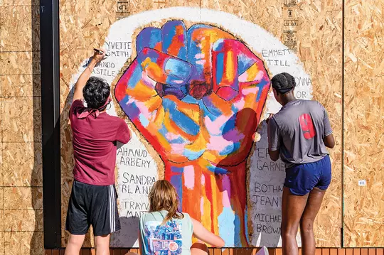 Students painting murals on State Street 2020 over plywood from destroyed windows due to racial justice protests. The students write the names of victims of racial injustice murders such as Breonna Taylor, Emmett Till and George Floyd