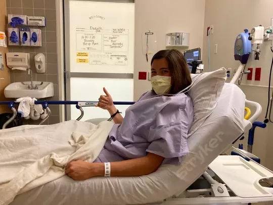 Danielle Hart resting in a hospital bed after ACL surgery and giving the thumbs up