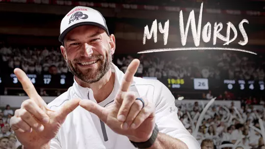 Joe Thomas, Wisconsin football and NFL alumnus, holds his hands in the "W" and smiles with the MyWords logo superimposed over the image
