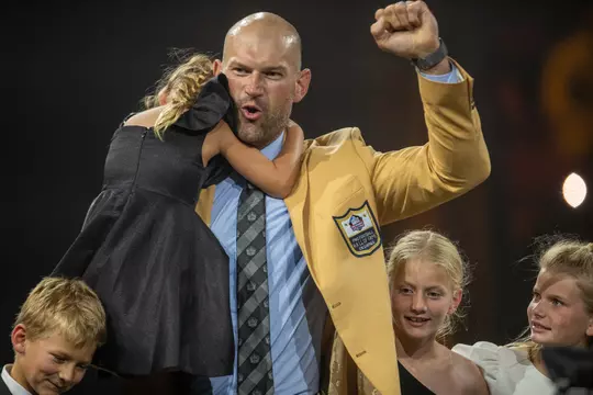 Joe Thomas, wearing his NFL Hall of Fame gold blazer jacket, cheers during the 2023 ceremony while holding his daughter and surrounded by his other three children who helped present him with the official enshrinement honor