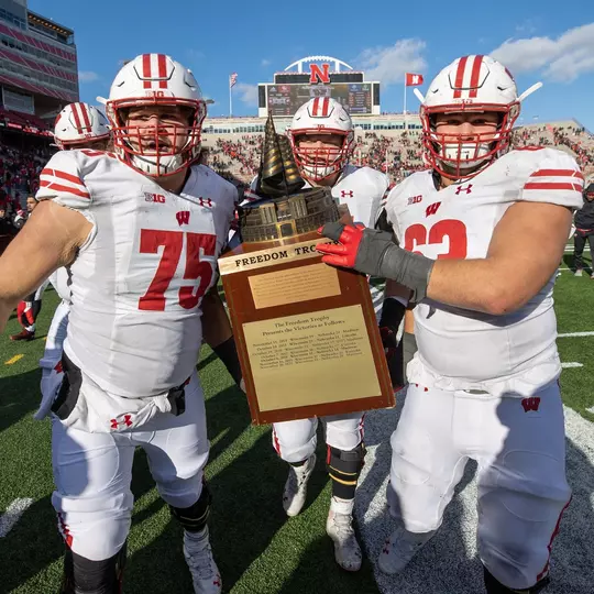 Wisconsin Badgers Joe Tippman (75) and Michael Furtney (74) and Tanor Bortolini (63) celebrate with the Freedom Trophy after an NCAA college football game against the Nebraska Cornhuskers, Sat., Nov. 19, 2022 in Lincoln, Nebraska. The Badgers won 15-14. (Photo by David Stluka/Wisconsin Athletic Communications)