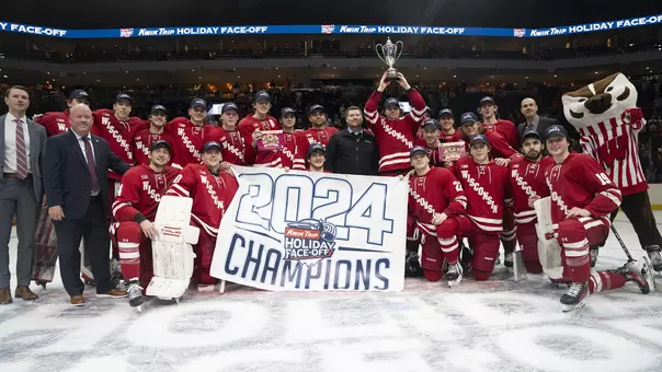 The Badger men's hockey team holding its 2024 Kwik Trip Holiday Face-Off banner and trophy