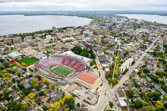 A sea of red- and white-attired fans fill Camp Randall Stadium at the University of Wisconsin–Madison as the Wisconsin Badgers play the Iowa Hawkeyes during a football game on Oct. 14, 2023. The aerial photograph was made from a helicopter looking northeast toward the isthmus and Wisconsin State Capitol during autumn with Lake Mendota on the left and Lake Monona on the right. (Photo by Jeff Miller / UW–Madison)
