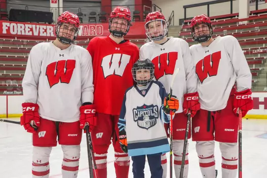 Ben Dexheimer, Quinn Finley, Jack Horbach and Kyle Kukkonen pose with a young Timber Wolves Hockey player with a Madison Capitols jersey on