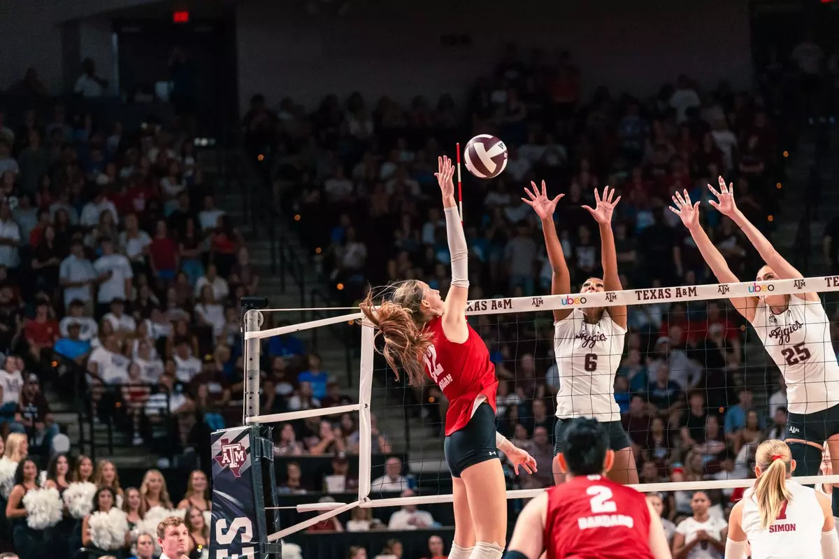 Wisconsin middle blocker Natalie Wardlow (#12) leaps high near the net to spike the ball past two Texas A&M defenders.