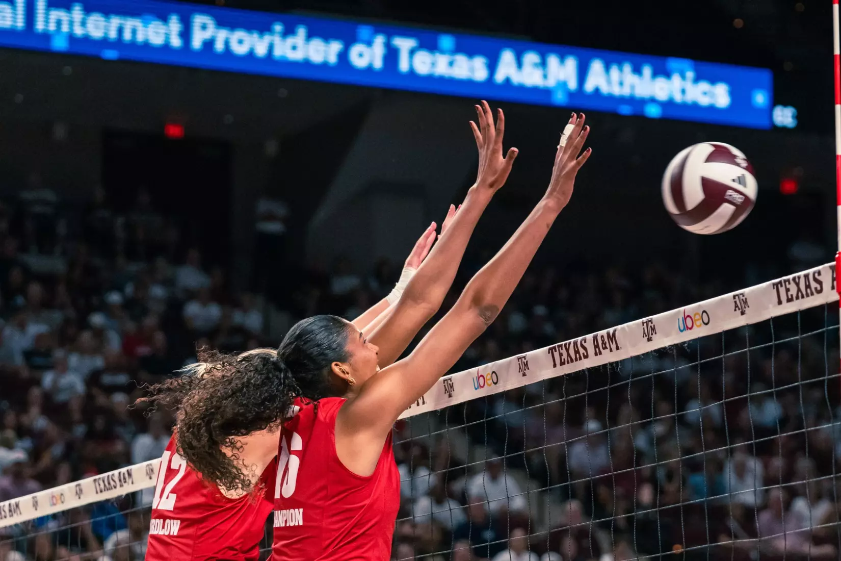 Wisconsin players Natalie Wardlow (#12) and Decelise Champion (#16) jump with hands extended high to block an attack at the net against Texas A&M.