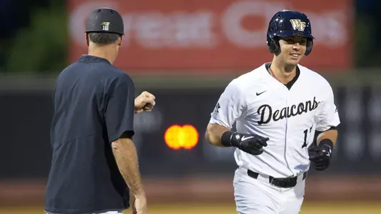 Bruce Steel (17) of the Wake Forest Demon Deacons bumps fists with head coach Tom Walter (16) as he rounds third base after hitting a home run against the Davidson Wildcats at David F. Couch Ballpark on May 7, 2019 in Winston-Salem, North Carolina. The Demon Deacons defeated the Wildcats 11-8. (Brian Westerholt/Four Seam Images)