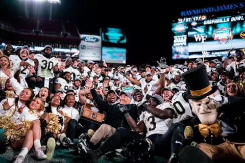 Photo of the football team, cheer team, and Demon Deacon mascot celebrating on the field with the trophy