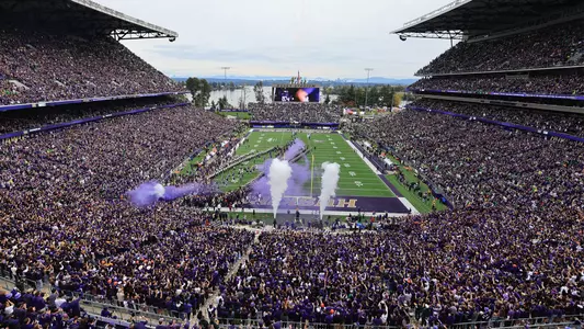 Wide shot of packed Husky Stadium during UW football runout with purple smoke