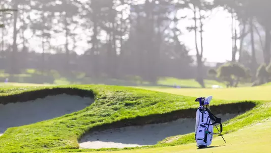 Men's golf bag sitting next to bunker