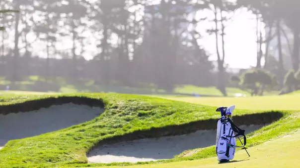 Men's golf bag sitting next to bunker