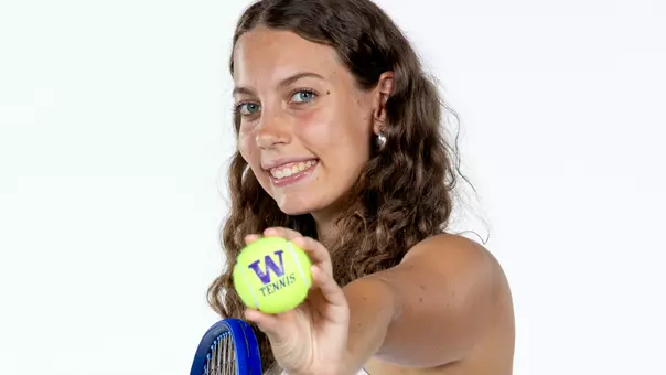 Alexia Jacobs holds a tennis ball to the camera with a W and tennis written on it