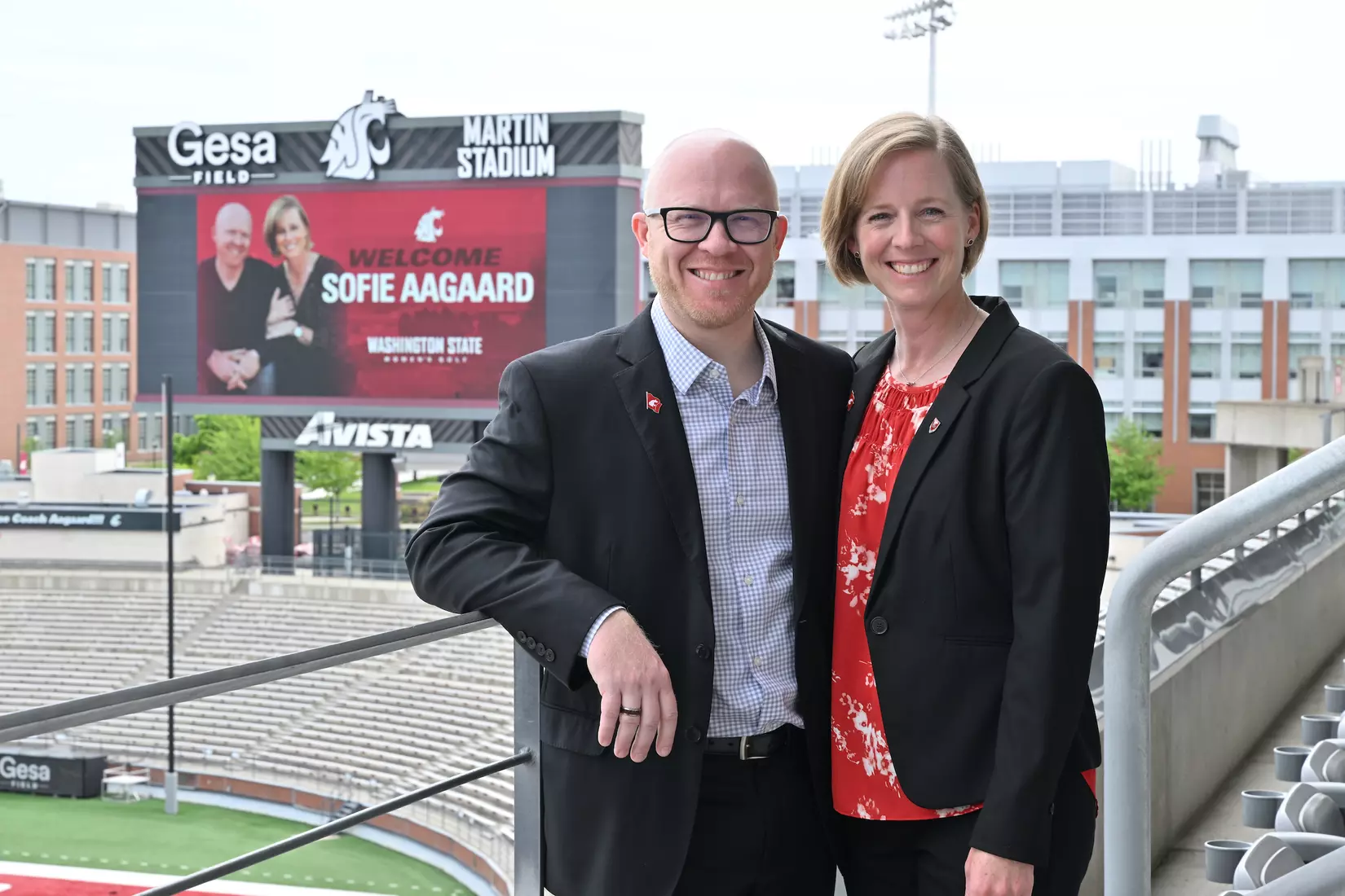 Sofia Aagaard and husband Christian standing out on the balcony of the Gesa Field Club seats in front of the videoboard with a welcome sign for coach Aagaard.