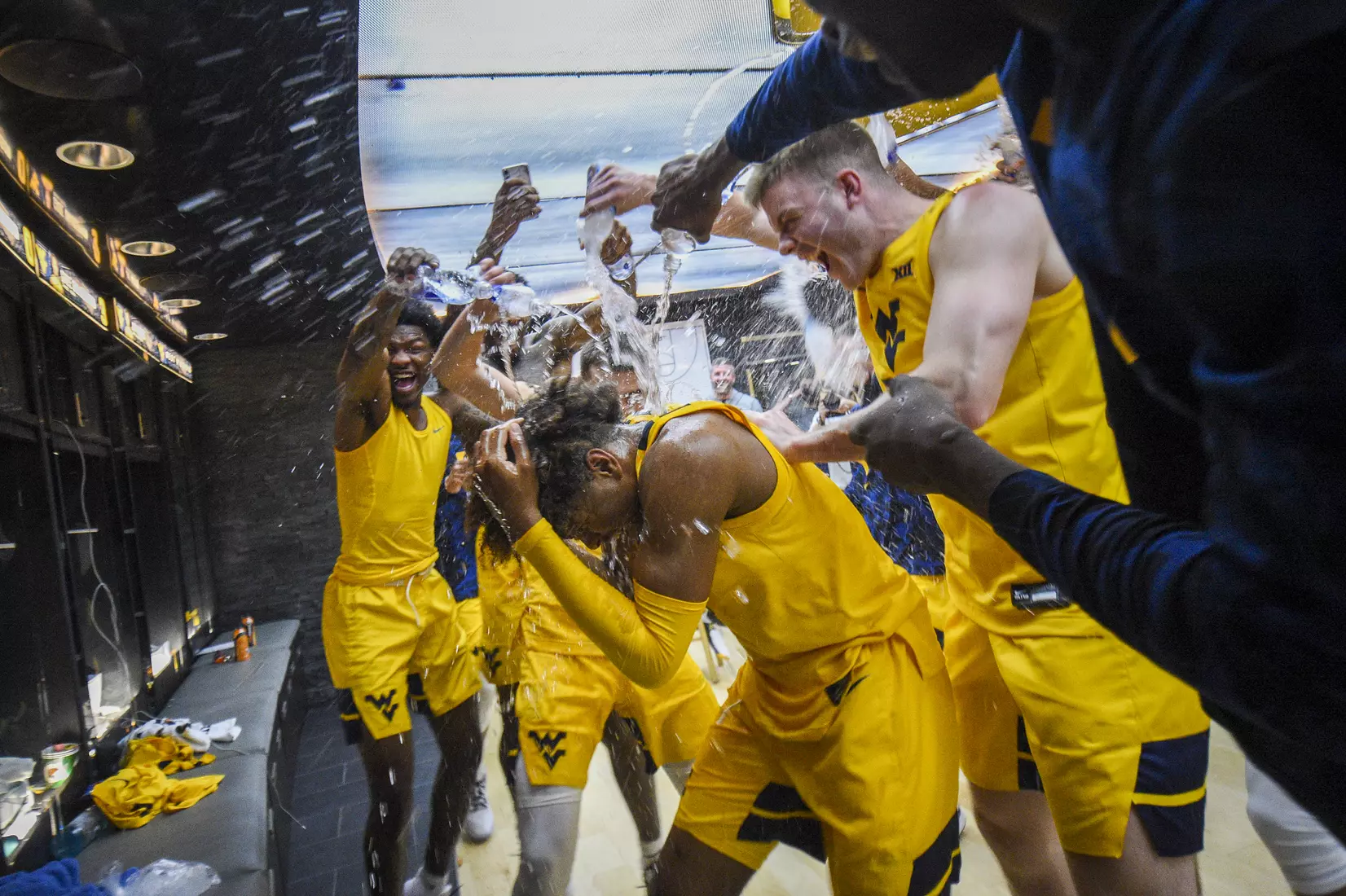Teammates shower Miles McBride with bottled water as he enters the postgame locker room.