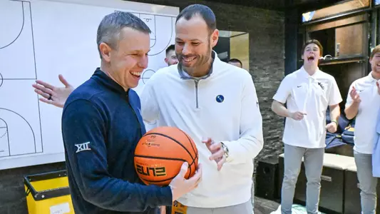 Athletic Director Wren Baker presents Ross Hodge with a basketball following a WVU men's basketball game.