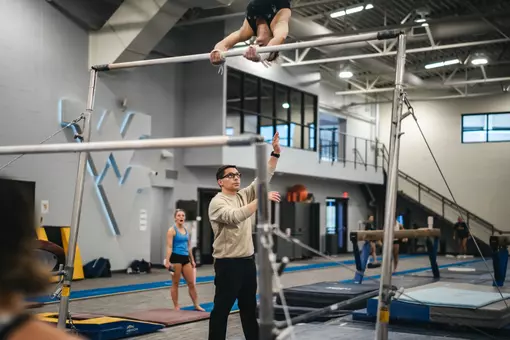 WVU gymnastics coach Jason Butts assists an athlete during practice at Cary Gym in Morgantown