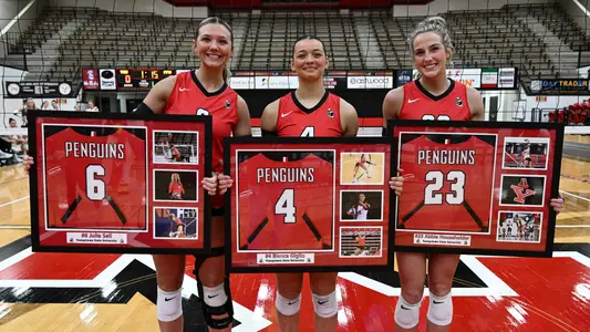 Senoirs Julia Sell, Bianca Giglio and Abbie Householder pose in front of the net holding framed jerseys on their Senior Day with the Youngstown State volleyball program. Photo by Robert Hayes.