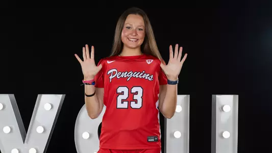 Gemma Walker pulls her jersey forward in front of a YSU sign in a photo studio setting