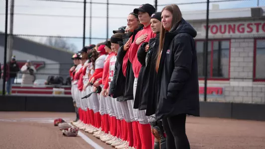 The Youngstown State softball team lines up along the third-base line to hear the National Anthem